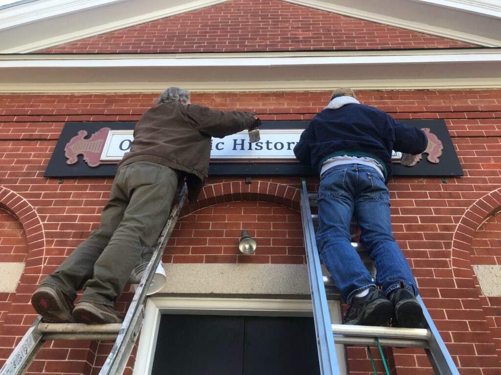 Two Men Fixing Old Mystic History Center Board